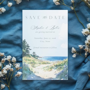 May include: A Save the Date card with a watercolor illustration of a coastal path leading to the ocean. The text reads "Save the Date" and announces the wedding of Sophie & Tyler on June 27, 2026, in City, State. Formal invitation to follow.