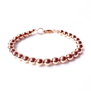 May include: A rose gold beaded bracelet with a lobster clasp closure.
