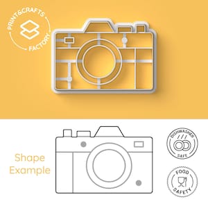 May include: White plastic camera cookie cutter with a line drawing of a camera on a yellow background. The cookie cutter is dishwasher and food safe.