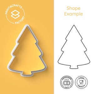 Op de afbeelding: Een witte omtrek van een kerstboomvorm op een gele achtergrond. De omtrek is een koekjesvormer met een schaduw. De tekst "Print & Crafts Factory" staat in een cirkel boven de koekjesvormer. Onder de koekjesvormer bevinden zich twee pictogrammen: "Dishwasher Safe" en "Food Safety".