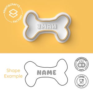 Peut inclure: Un emporte-pièce blanc en forme d'os de chien avec le mot "NAME" au centre. Le découpoir a un contour doré et se trouve sur un fond jaune. L'image comprend également le texte "PRINT & CRAFTS FACTORY", "Shape Example" et des icônes indiquant le lave-vaisselle et la sécurité alimentaire.