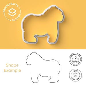 Puede incluir: Un cortador de galletas de plástico blanco con forma de gorila. El cortador se muestra sobre un fondo amarillo. Un dibujo de línea del gorila se muestra debajo del cortador. El texto "Print & Crafts Factory" se muestra en un círculo sobre el cortador. El texto "Shape Example" se muestra debajo del dibujo de línea. Dos iconos se muestran a la derecha del dibujo de línea. El primer icono es un círculo con el texto "Dishwasher Safe" y una imagen de dos platos. El segundo icono es un círculo con el texto "Food Safety" y una imagen de un vaso y un tenedor.