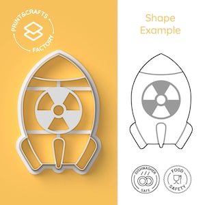 Peut inclure: Emporte-pièce en plastique blanc en forme de fusée avec un symbole de radiation sur le côté. L'emporte-pièce est sur un fond jaune. L'image montre également un dessin au trait de l'emporte-pièce, des icônes de sécurité lave-vaisselle et alimentaire.