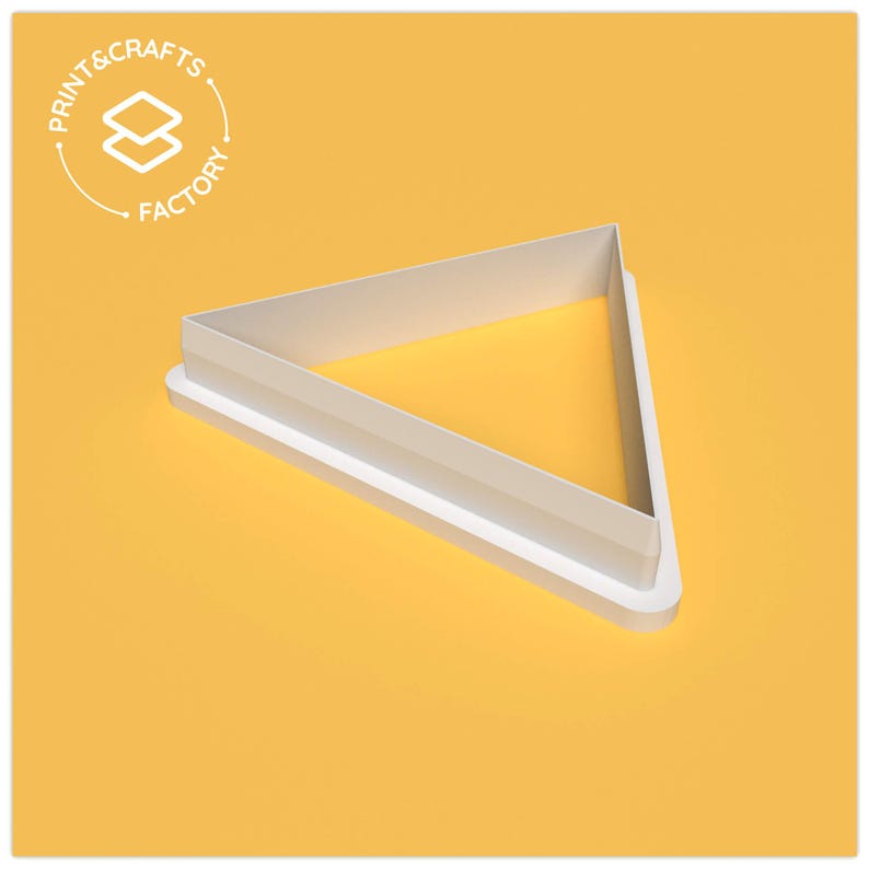 Puede incluir: Un cortador de galletas triangular blanco con una base redondeada, sobre un fondo amarillo. El cortador es de "Print & Crafts Factory". El dise&ntilde;o es una forma geom&eacute;trica simple, ideal para hornear o hacer manualidades.