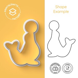 Op de afbeelding: Een witte koekjesvorm in de vorm van een zeehond op een gele achtergrond. De afbeelding bevat een zwarte omtrek met het label Shape Example, een Print & Crafts Factory logo en ronde iconen voor Dishwasher Safe en Food Safety.
