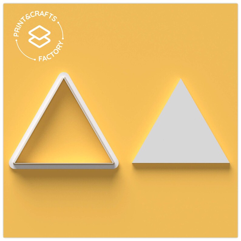 Puede incluir: Dos cortadores de galletas triangulares blancos sobre un fondo amarillo. Uno es un marco, el otro un tri&aacute;ngulo s&oacute;lido. El logotipo de Print & Crafts Factory est&aacute; en la esquina superior izquierda.