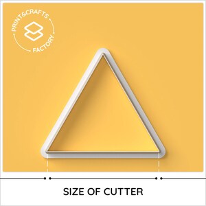 Puede incluir: Un cortador de galletas blanco en forma de tri&aacute;ngulo sobre un fondo amarillo. El cortador est&aacute; delineado en blanco y relleno de amarillo. El texto "PRINT & CRAFTS FACTORY" est&aacute; en un c&iacute;rculo en la esquina superior izquierda. El texto "SIZE OF CUTTER" est&aacute; en la parte inferior.