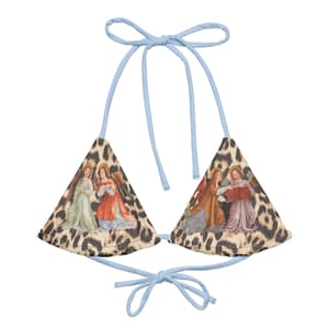Può includere: Un top bikini triangolare di colore azzurro con uno sfondo a stampa leopardata e un dipinto di tre angeli su ogni lato.