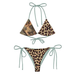 May include: A light blue bikini with a leopard print bottom and a top with a vintage illustration of an angel on one side and a leopard print on the other side.
