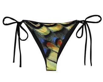 May include: A black bikini bottom with a butterfly wing pattern. The pattern features yellow, blue, and orange hues. The bikini bottom has black ties on each side.