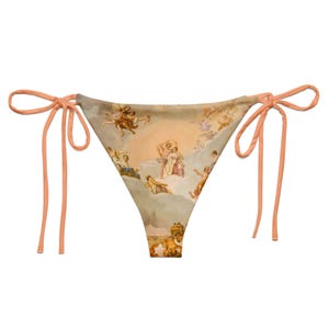 May include: A bikini bottom featuring a Renaissance-style painting of cherubs and figures in a cloudy sky. The bikini has peach-colored tie strings on each side. The overall color palette includes beige, peach, and muted tones.