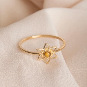 Pode incluir: Um anel de ouro com um delicado design de flor que apresenta uma gema amarela no centro.