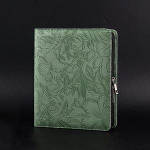 May include: A sage green zippered folio with an embossed floral pattern. The design features detailed leaves and flowers. The zipper is black with a silver-toned pull. The folio is closed and appears to be made of leather or a similar material.