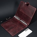 May include: A dark burgundy leather binder featuring a six-ring metal mechanism, a snap-button closure strap, and multiple interior card slots. The binder is accompanied by a black ballpoint pen and a white smartphone placed on the surface.