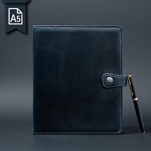 May include: A5 dark blue leather journal with a silver clasp and a black pen with gold accents. The journal has a stitched border and a matching blue closure. A white A5 icon is in the upper left corner.