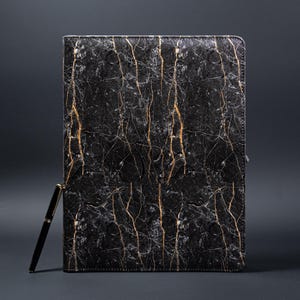 May include: Black leather laptop sleeve with a gold marble pattern. The sleeve has a zipper closure and a pen holder.