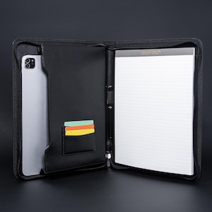 以下が含まれることがあります： 黒い革製ポートフォリオ。ジッパー開閉式で、タブレット、罫線入りのメモ帳、カードスロットが現れます。ビジネスや個人使用に最適な、様々なアイテムを収納できるデザインです。