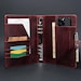 May include: A dark burgundy leather binder featuring a six-ring metal mechanism, multiple interior card slots, a vertical pocket containing a smartphone, and a side pen loop. The organizer includes various paper inserts with printed text.