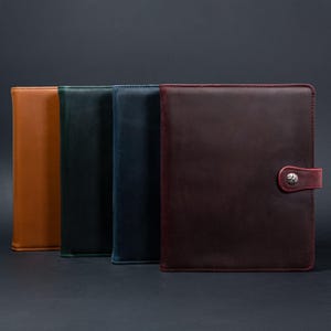 Op de afbeelding: Vier lederen notitieboekjes in verschillende kleuren: bruin, groen, blauw en bordeauxrood. Het bordeauxrode notitieboekje heeft een zilveren knoopsluiting.