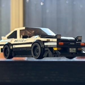 May include: A white and black Lego model of a Toyota AE86 Trueno with the Japanese text "藤原とうふ店" on the side and a number plate that reads "Gunma 13-954".