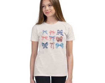 May include: A white youth-sized t-shirt with a design of nine colorful bows in red, white, and blue. The bows are arranged in a grid pattern.