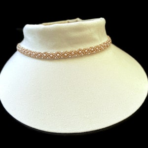 May include: A white fabric choker necklace with a beaded trim. The beads are a light peach color.