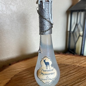 May include: A decorative glass bottle with a silver-wrapped neck and a white wax seal. The bottle has a label that reads "Pensieve Memories" with a deer silhouette and the text "Severus Snape 1998". A silver chain and charm hang from the neck.