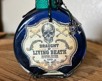 May include: A dark blue potion bottle with a label reading "Draught of Living Death." The label features a skull and crossbones design. The bottle is sealed with green wax and has a skull charm attached. The text "USE WITH CAUTION" is visible.