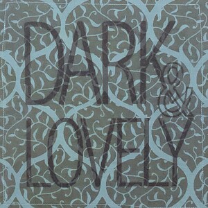 May include: Square cloth napkin featuring a teal and grey floral design. The words "DARK & LOVELY" are printed in dark grey across the centre. The edges are finished with a white stitch.