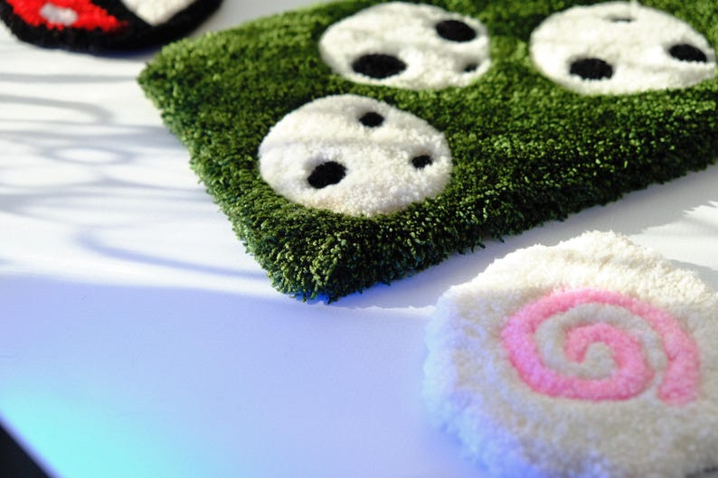 May include: A green, textured rug with white and black panda face designs. A white rug with a pink and white spiral design is also visible. The rugs are made of a soft, plush material.