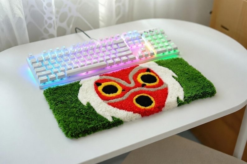 May include: A white mechanical keyboard with multi-coloured LED lights rests on a green and red rug with a character design. The rug has a green border and a red and white face design.