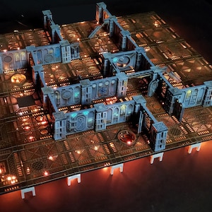 Peut inclure: Un ensemble de terrain de jeu de table détaillé, avec une conception modulaire avec des couloirs et des pièces interconnectés. L'ensemble est principalement marron et gris, avec des accents bleus et des sections éclairées. Le texte "GOTHIC SECTOR: LOST SHIPS" est visible.