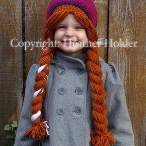 May include: A young person wearing a gray coat with a purple, orange, and brown crocheted hat with long orange and white yarn braids.
