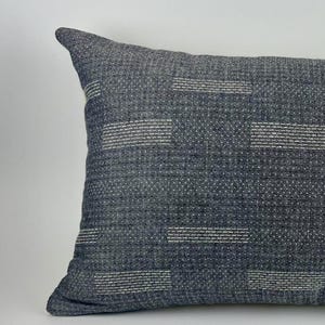 Könnte beinhalten: Rechteckiges Zierkissen in Blau- und Grautönen. Das Kissen hat einen strukturierten Stoff mit horizontalen weißen Streifenmustern. Das Kissen ist etwa 51 cm lang und 30 cm breit.