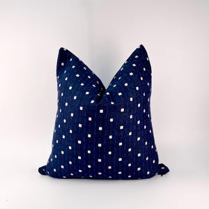 May include: Square throw pillow with a navy blue fabric featuring a pattern of small white squares. The pillow is a decorative accent for a bed or sofa, adding a touch of color and texture to any room.