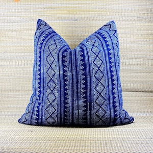 May include: A square cushion in a deep blue hue, adorned with a white geometric pattern. The design includes vertical stripes and diamond shapes, creating a symmetrical look. This cushion is a decorative item, suitable for a bed or sofa.