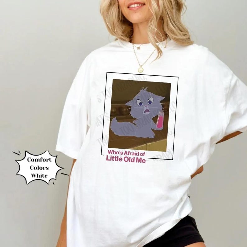 May include: White t-shirt with a cartoon cat holding a pink bottle. The text "Who's Afraid of Little Old Me" is printed below the image.
