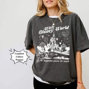 May include: A dark grey t-shirt featuring a white graphic of the Walt Disney World castle and Mickey Mouse. The text "Walt Disney World" and "The happiest place on earth" are also printed on the shirt.