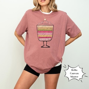 K&ouml;nnte beinhalten: Ein mauvefarbenes Bella Canvas T-Shirt mit einer Grafik eines Dessert-Sundae mit dem Text "geschnittene Bananen, ein wenig Pudding, geschichtet mit Birne und mehr, mehr Ladyfinger, Himbeeren, Pudding aus eigener Herstellung, Schicht aus Ladyfingern".