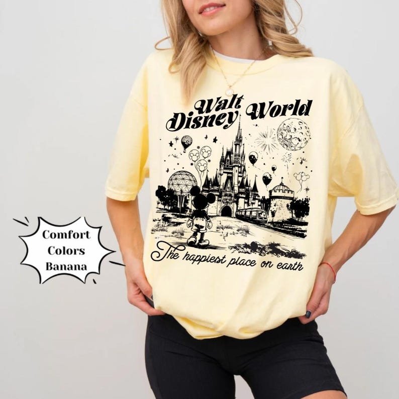 May include: A yellow t-shirt featuring a black and white illustration of Cinderella's castle and Mickey Mouse. The text "Walt Disney World" and "The happiest place on earth" are printed on the shirt.