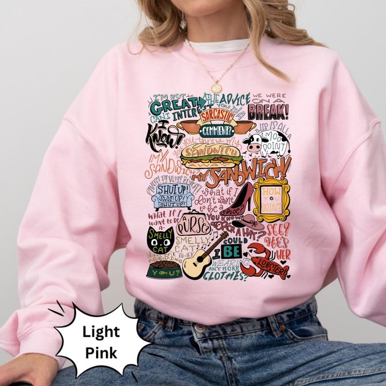 Op de afbeelding: Een lichtroze sweatshirt met een grafische print van verschillende zinnen en afbeeldingen uit de populaire tv-serie "Friends". De print bevat zinnen als "Ik weet", "We waren uit elkaar", "Mijn sandwich", "Hoe gaat het?" en "Stinkende kat".