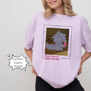 May include: A lavender t-shirt with a cartoon cat image and the text "Who's Afraid of Little Old Me".