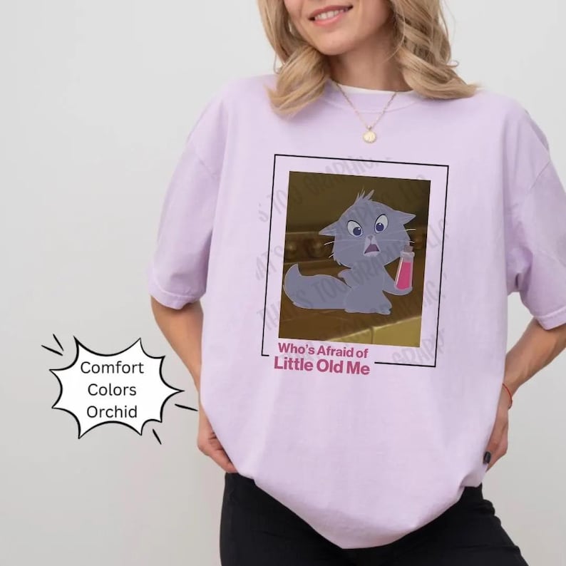 May include: A lavender t-shirt with a cartoon cat image and the text "Who's Afraid of Little Old Me".