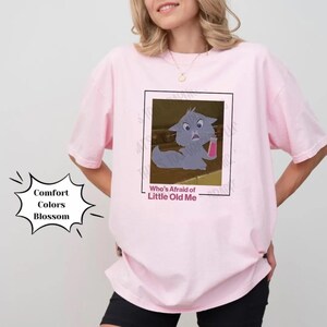 May include: Pink t-shirt with a graphic of a cartoon cat holding a glass of pink liquid. The text "Who's Afraid of Little Old Me" is printed below the image.