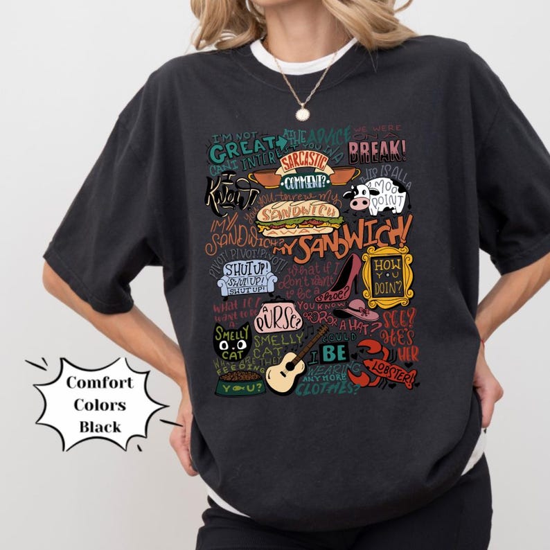 Op de afbeelding: Zwart T-shirt met een kleurrijke grafische print van verschillende zinnen en afbeeldingen uit de populaire tv-serie "Friends". De grafiek bevat de tekst "Ik ben niet goed in dit", "Hoe gaat het?", "Draai", "Stinkende kat", "Mijn sandwich" en "We waren in een pauze!"