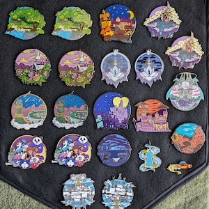 May include: A collection of 20 colorful enamel pins featuring various designs, including castles, landscapes, and characters. The pins are arranged in a grid pattern on a black fabric background.