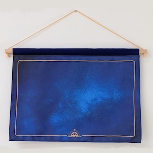 May include: A blue and gold tapestry with a starry night sky design. The tapestry is hanging on a wall with a wooden rod and string. The tapestry has a gold border and the text "Scales Tour" in the bottom center.