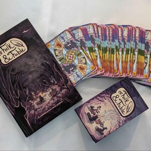 May include: A set of playing cards with a purple and gold design. The cards are in a stack and have a title that reads "Of Folk & Fable". A book with the same title is also pictured.