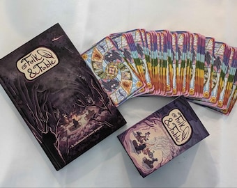 Pode incluir: Um baralho de cartas com um design roxo e dourado. As cartas estão empilhadas e têm um título que diz "Of Folk & Fable". Também é mostrado um livro com o mesmo título.