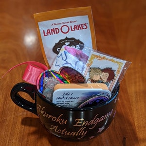 May include: A black mug filled with gifts, including a Land O Lakes cocoa packet, a pink ribbon, and various pins and cards. The mug has the text "Akuroku Endgame Actually" in gold lettering.